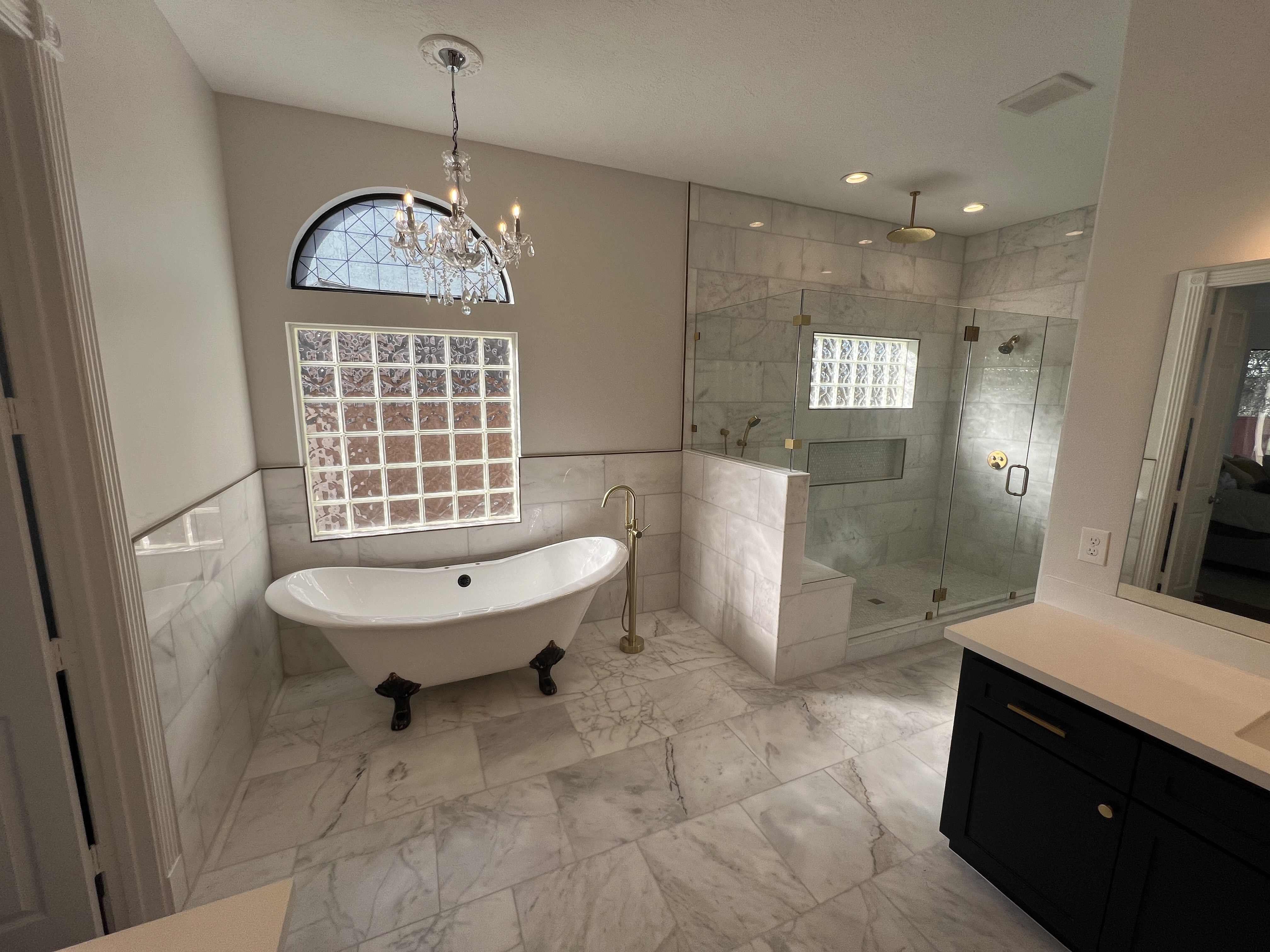 Luxury bathroom renovation by GT Holdings — clawfoot tub, chandelier, marble tile