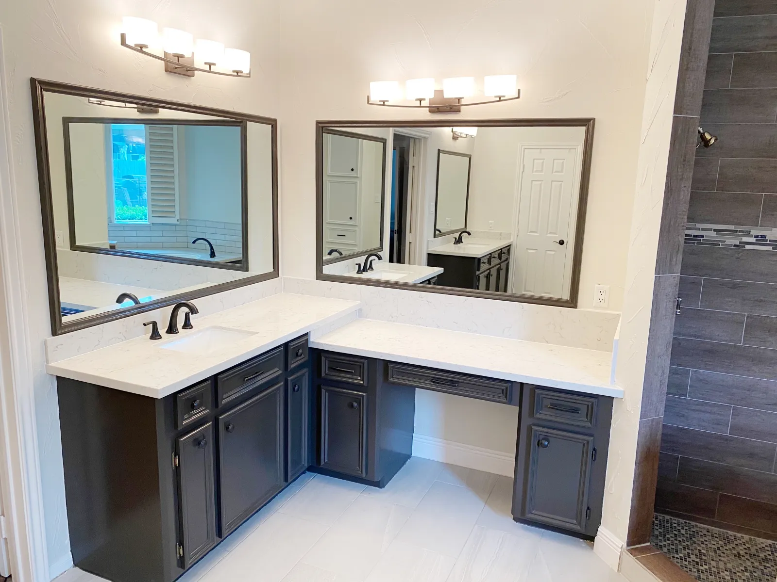 Remodeled L-shaped dual vanity with charcoal blue cabinetry, white quartz countertops, and oil-rubbed bronze fixtures
