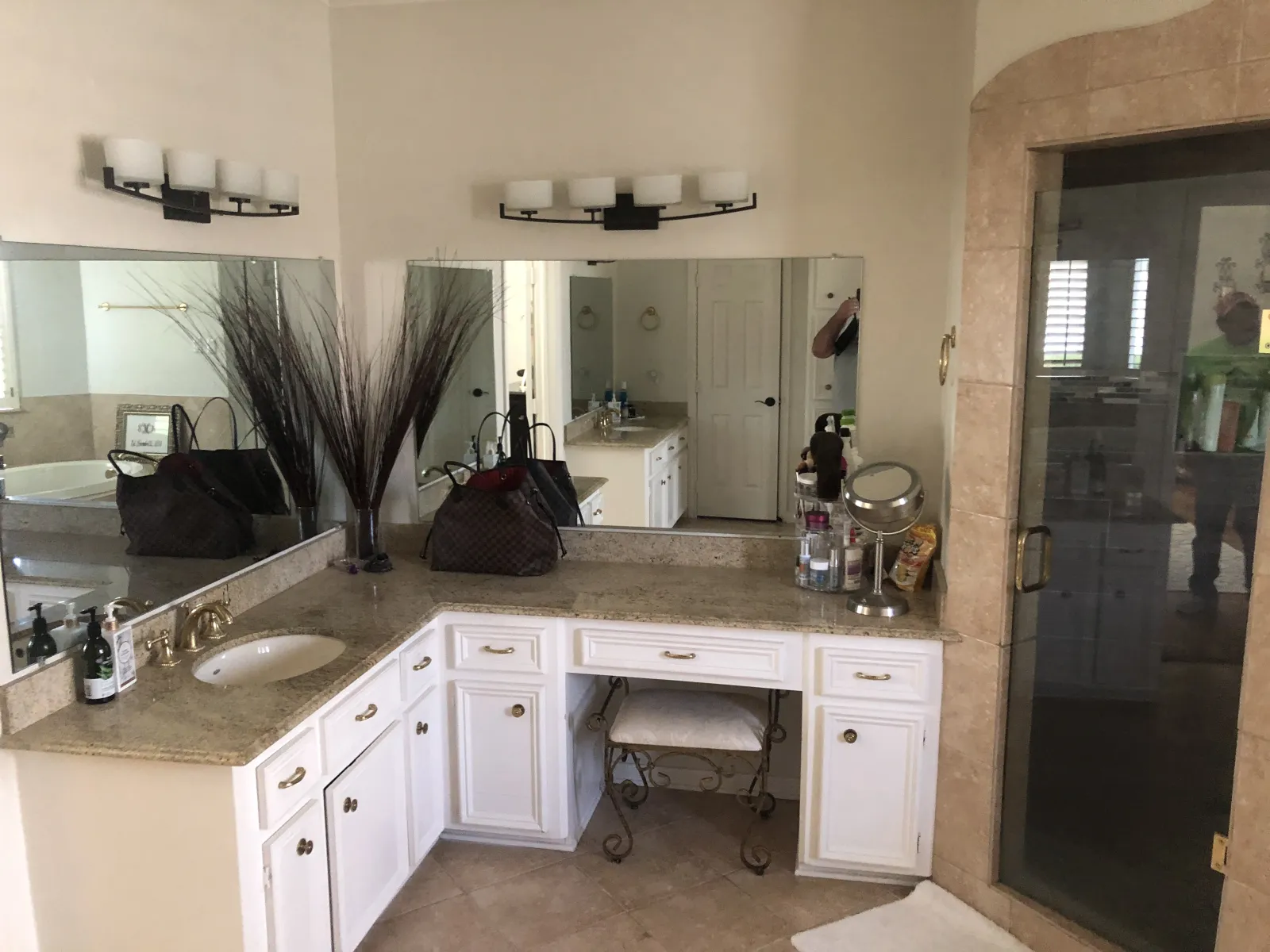 Outdated L-shaped bathroom vanity with white cabinetry, granite countertops, brass hardware, and a seated makeup area