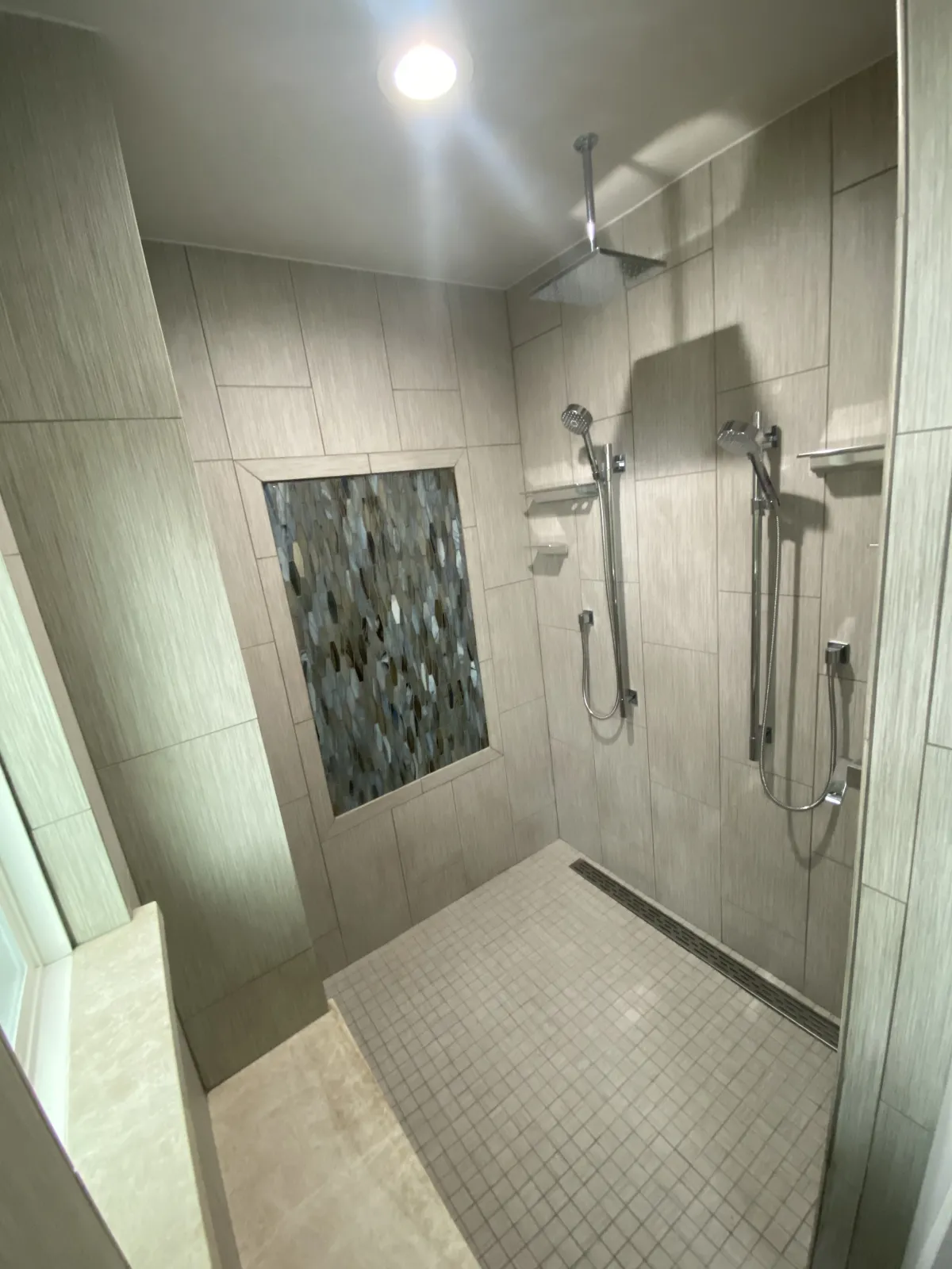Renovated walk-in shower with large-format linear tile, river rock pebble floor, chrome dual showerheads, and mosaic accent niche