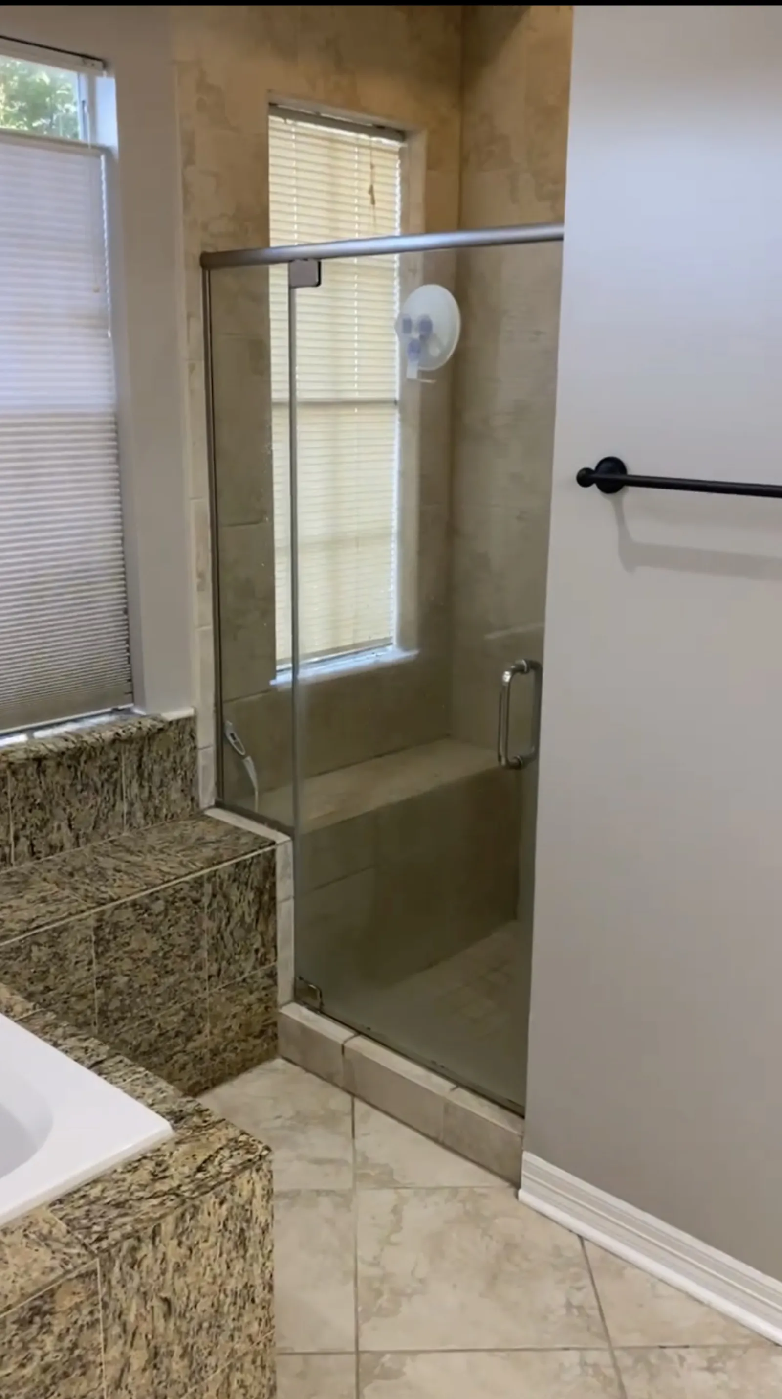 Existing bathroom with a glass shower door, beige stone tile surround, and granite-wrapped soaking tub