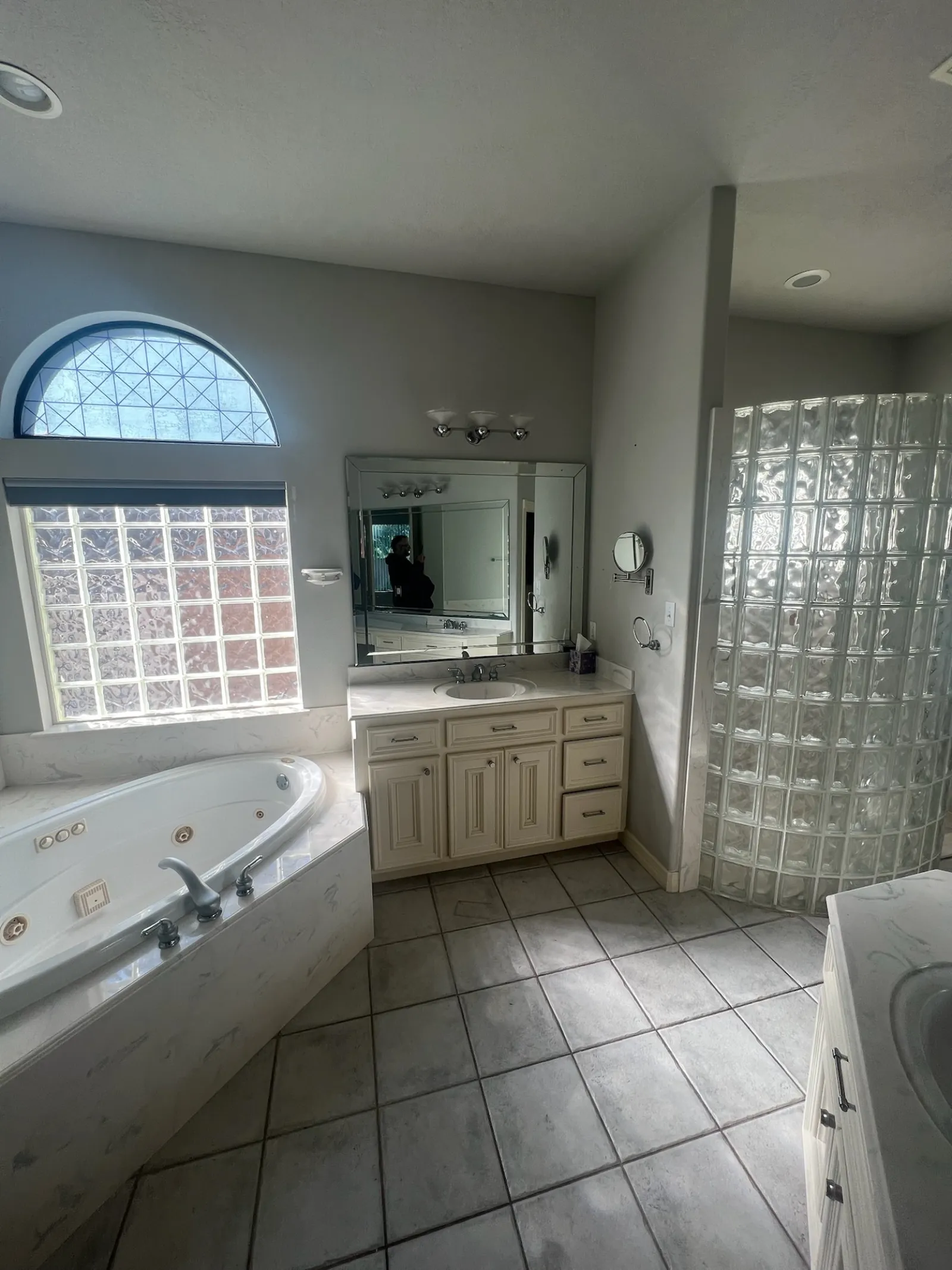 Dated master bathroom with a corner jetted tub, glass block window, and curved glass block shower wall
