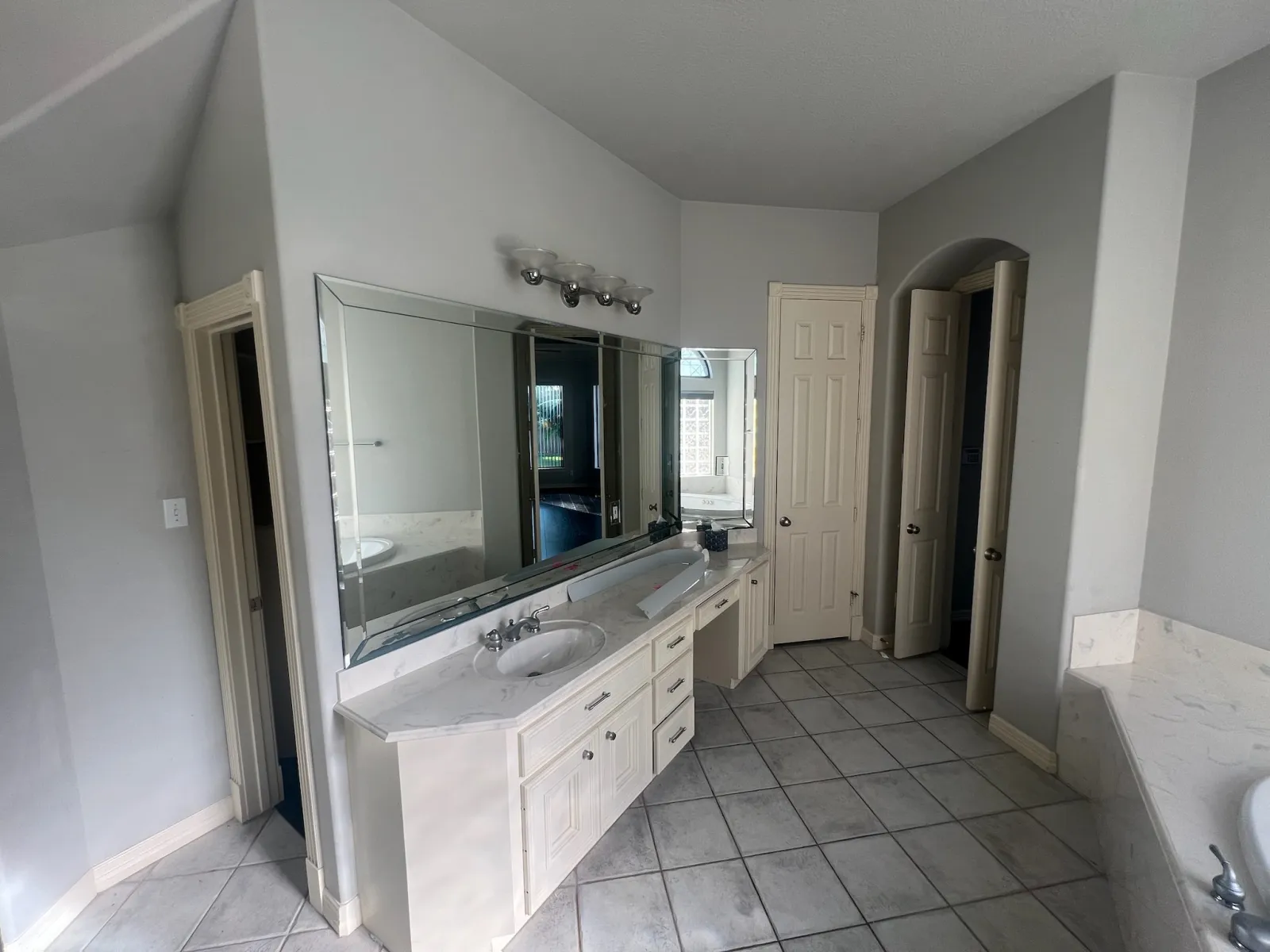 Original master bathroom vanity area with white cabinetry, marble countertop, and large frameless mirror