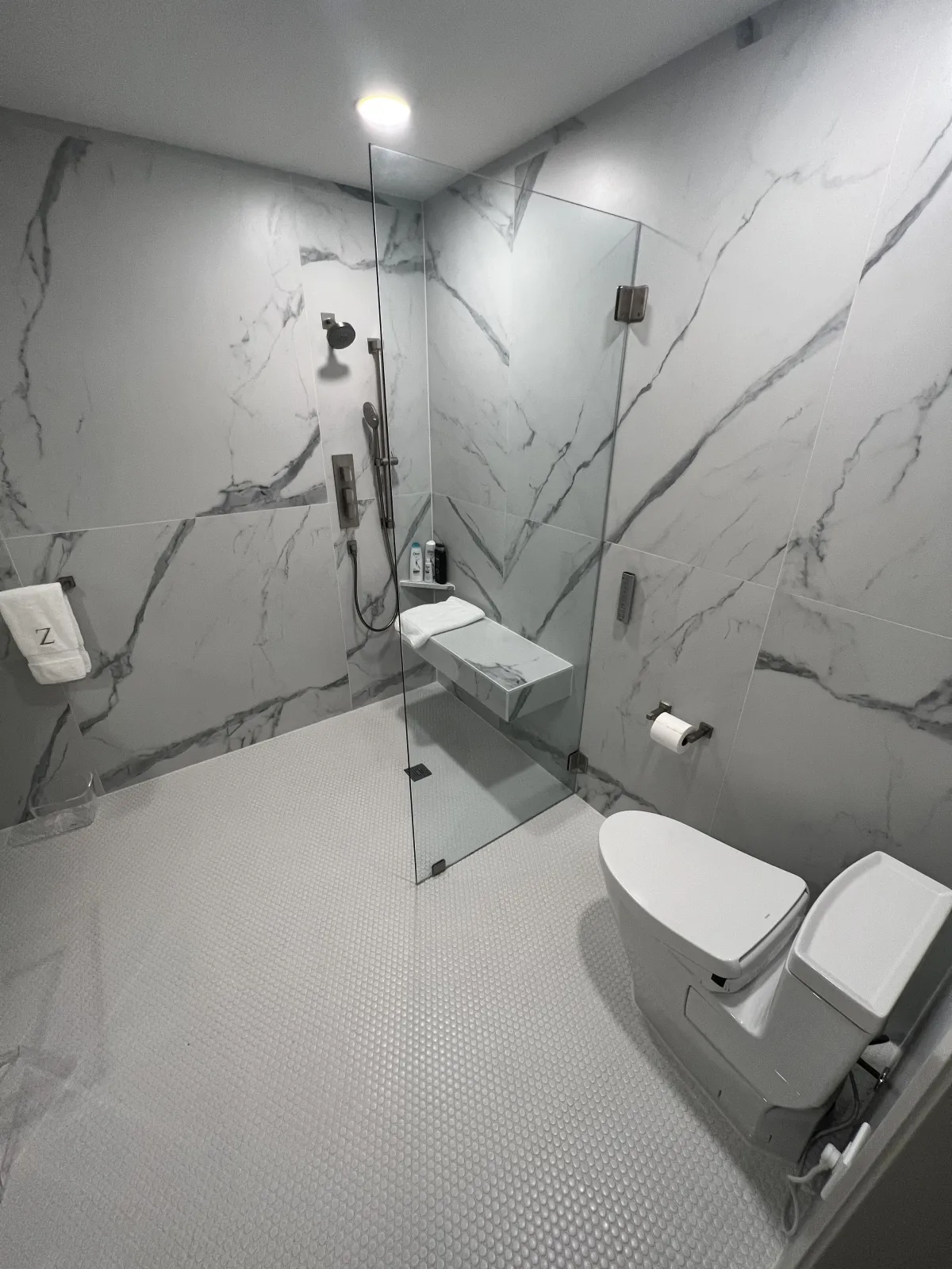 Renovated walk-in shower with dramatic white marble-look porcelain slab walls, frameless glass enclosure, and chrome fixtures
