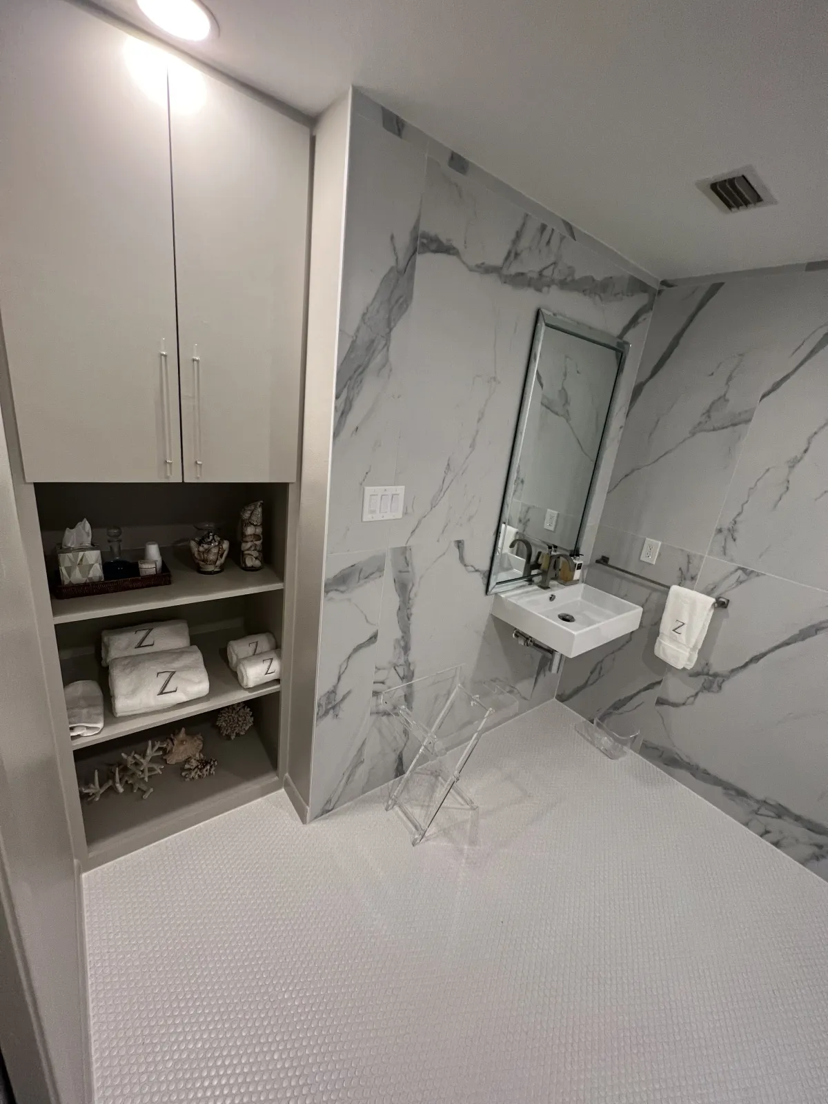 Remodeled bathroom vanity with a floating white cabinet, marble-look porcelain slab wall, and open shelving