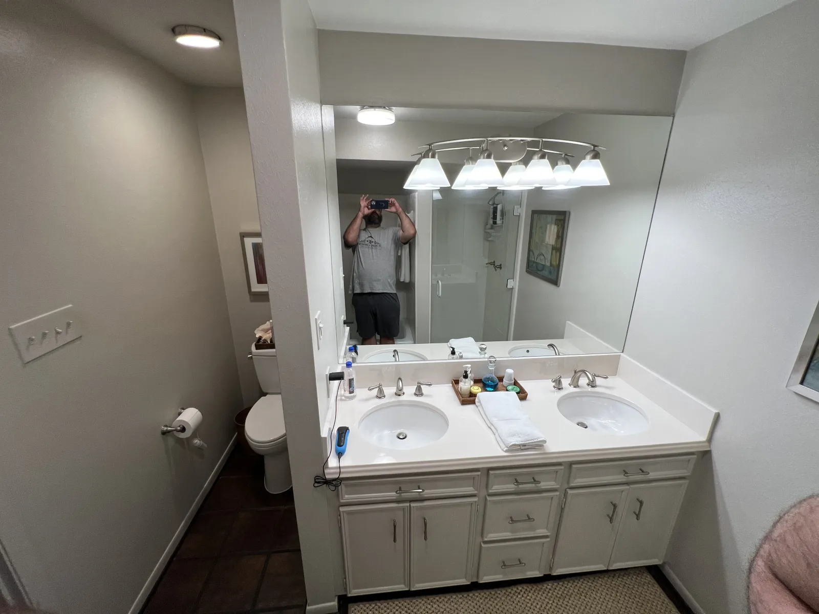 Dated bathroom with a white double-sink vanity, frameless wall mirror, and dark tile flooring