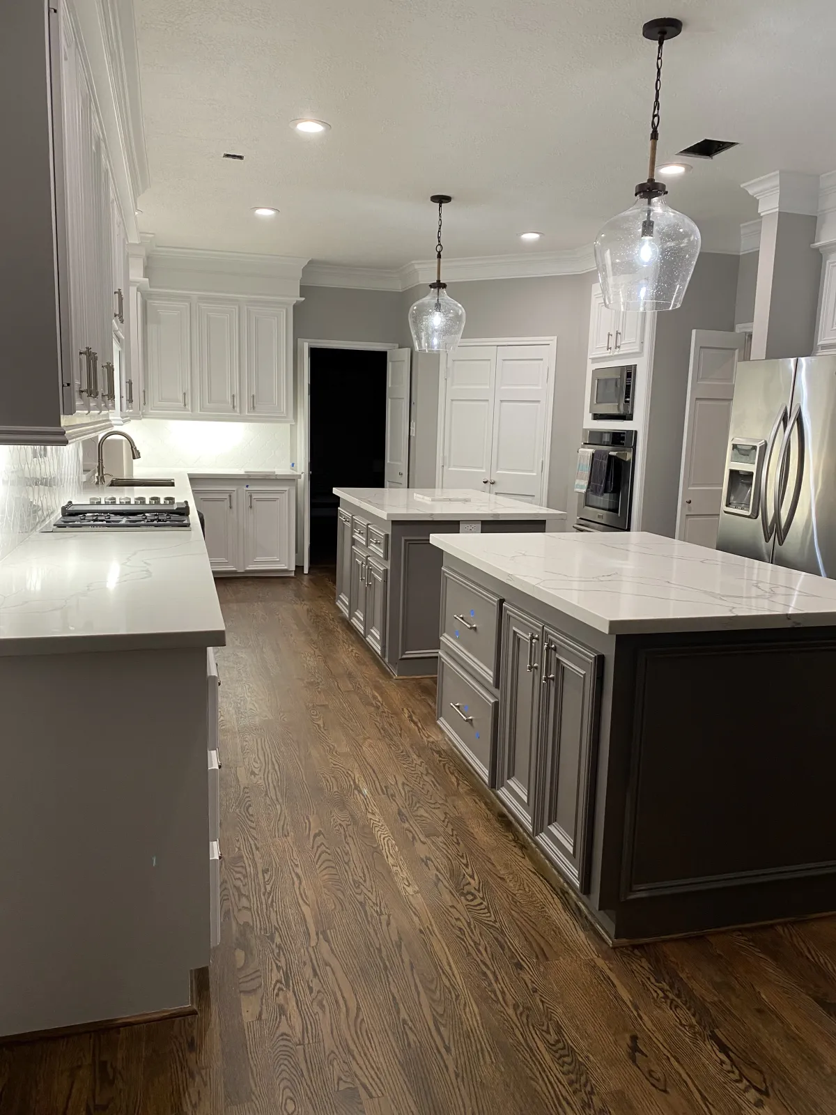 Completed remodeled kitchen with white raised-panel cabinets, quartz countertops, dark hardwood flooring, and a glass pendant light over the island