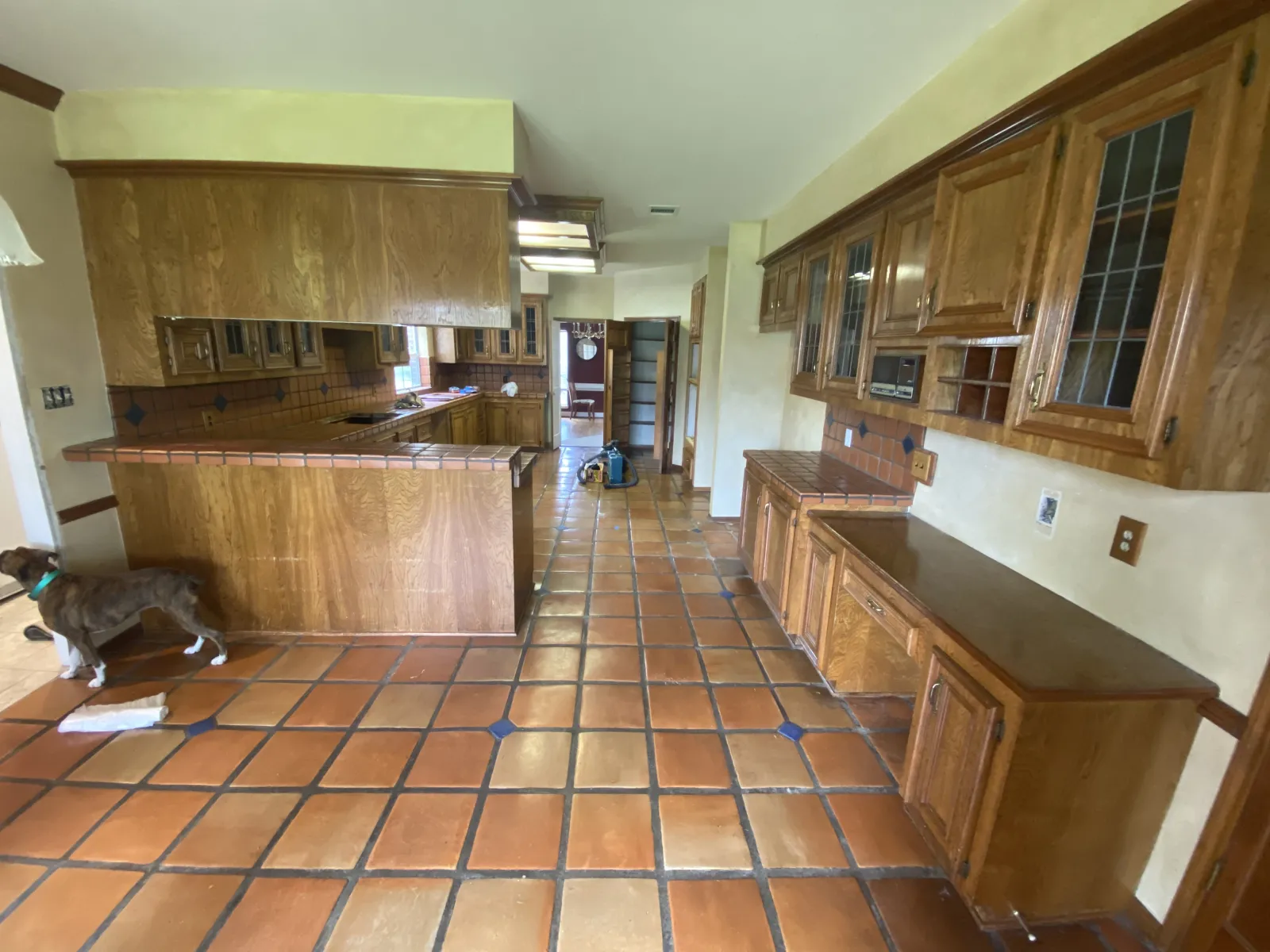 Outdated kitchen with honey oak cabinets, terracotta Saltillo tile flooring with blue diamond accents, and tile countertops before remodel