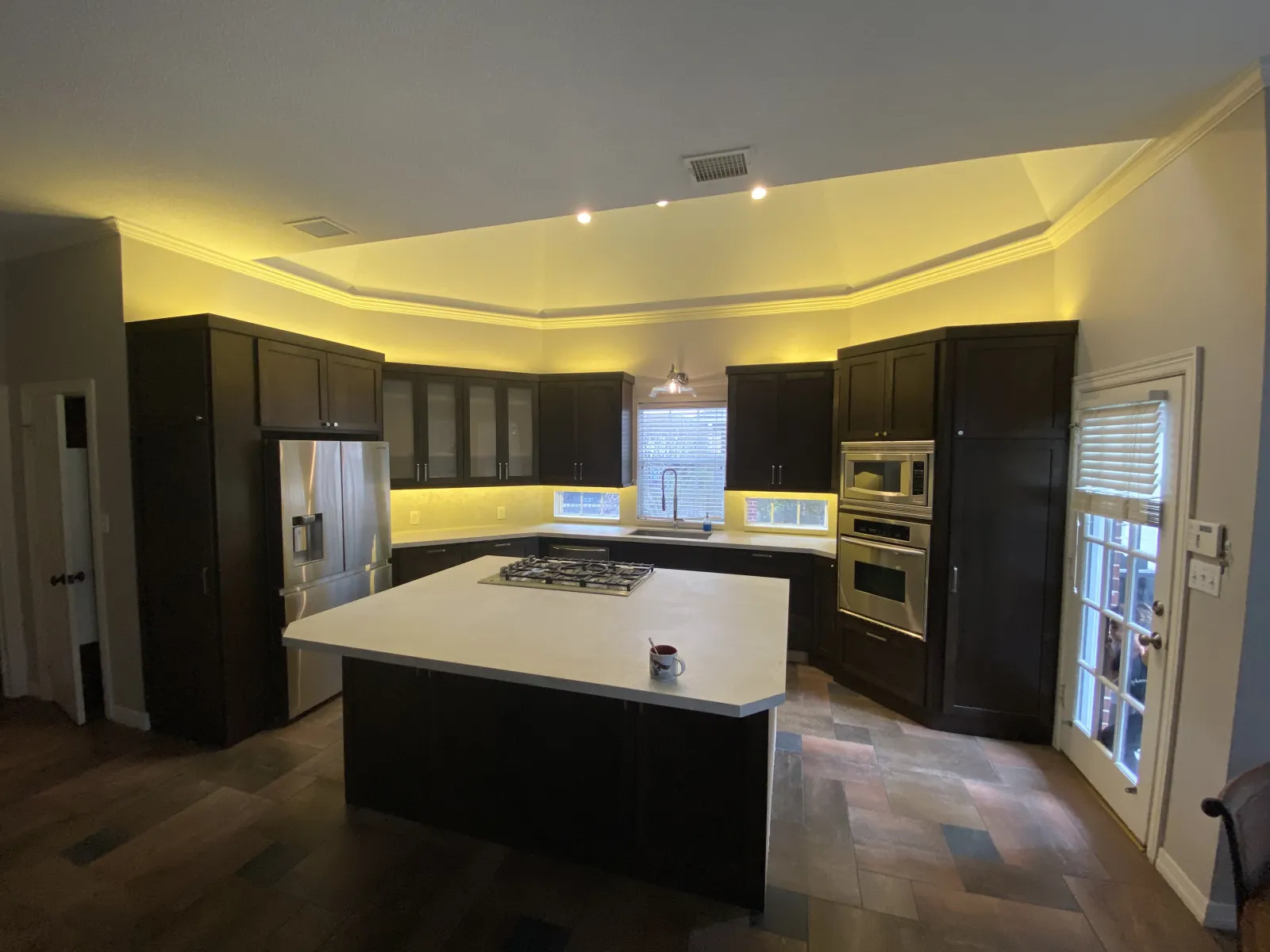 A dramatically transformed kitchen with dark espresso shaker cabinets, white quartz countertops, LED accent lighting, and a tray ceiling