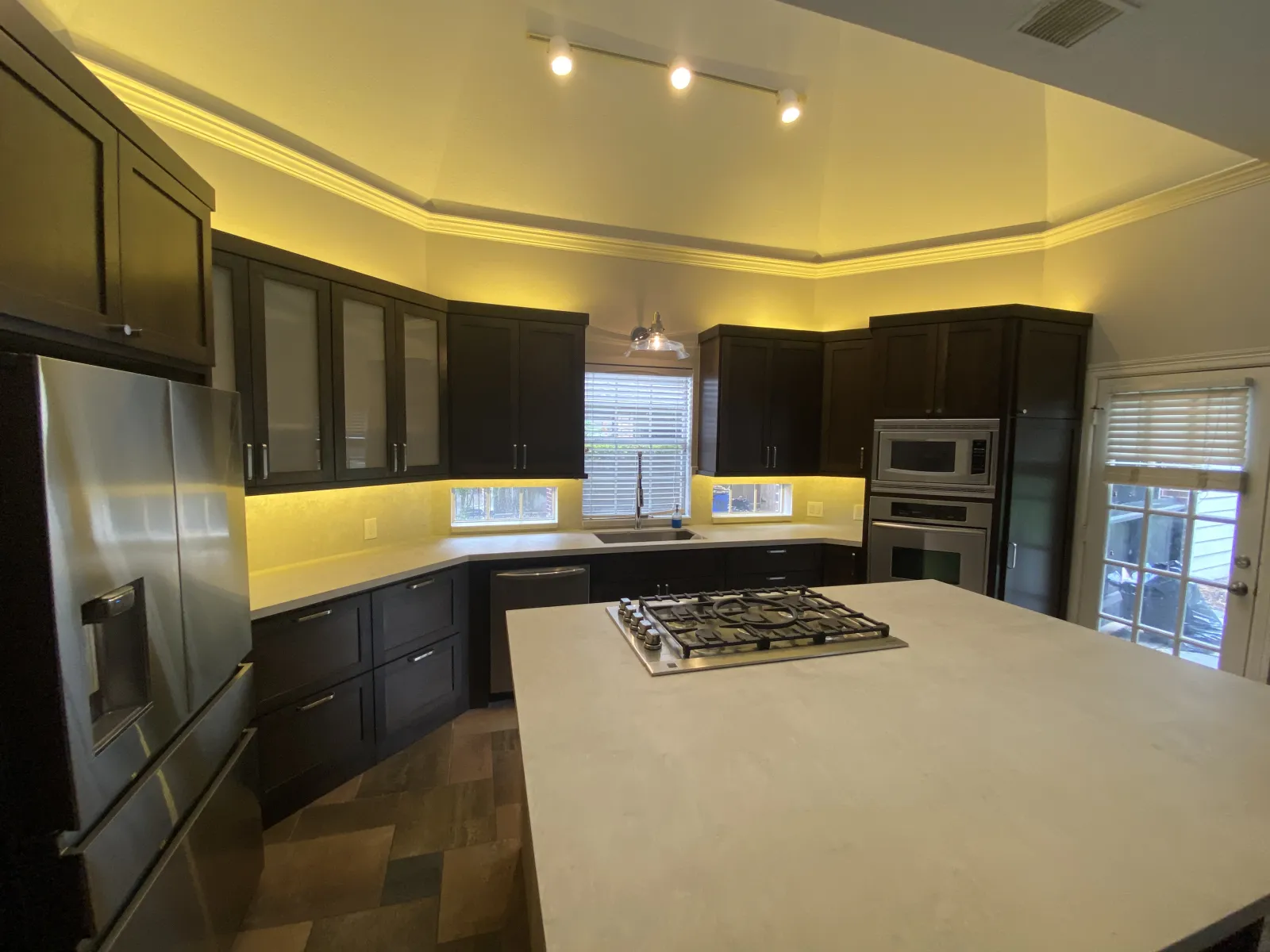 The completed espresso-toned kitchen from the opposite angle, showcasing the large quartz island with gas cooktop and frosted glass cabinet doors