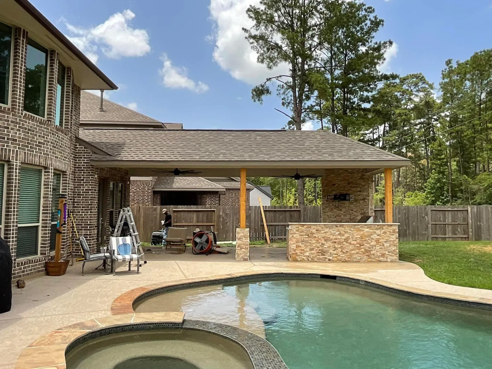 Completed covered patio with stone outdoor kitchen, cedar posts, and a pool in the foreground