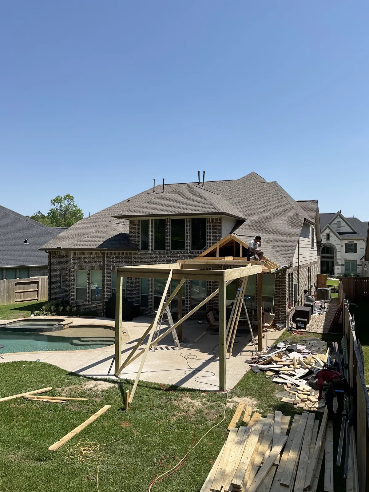 Wood framing for a covered patio structure under construction behind a two-story brick home