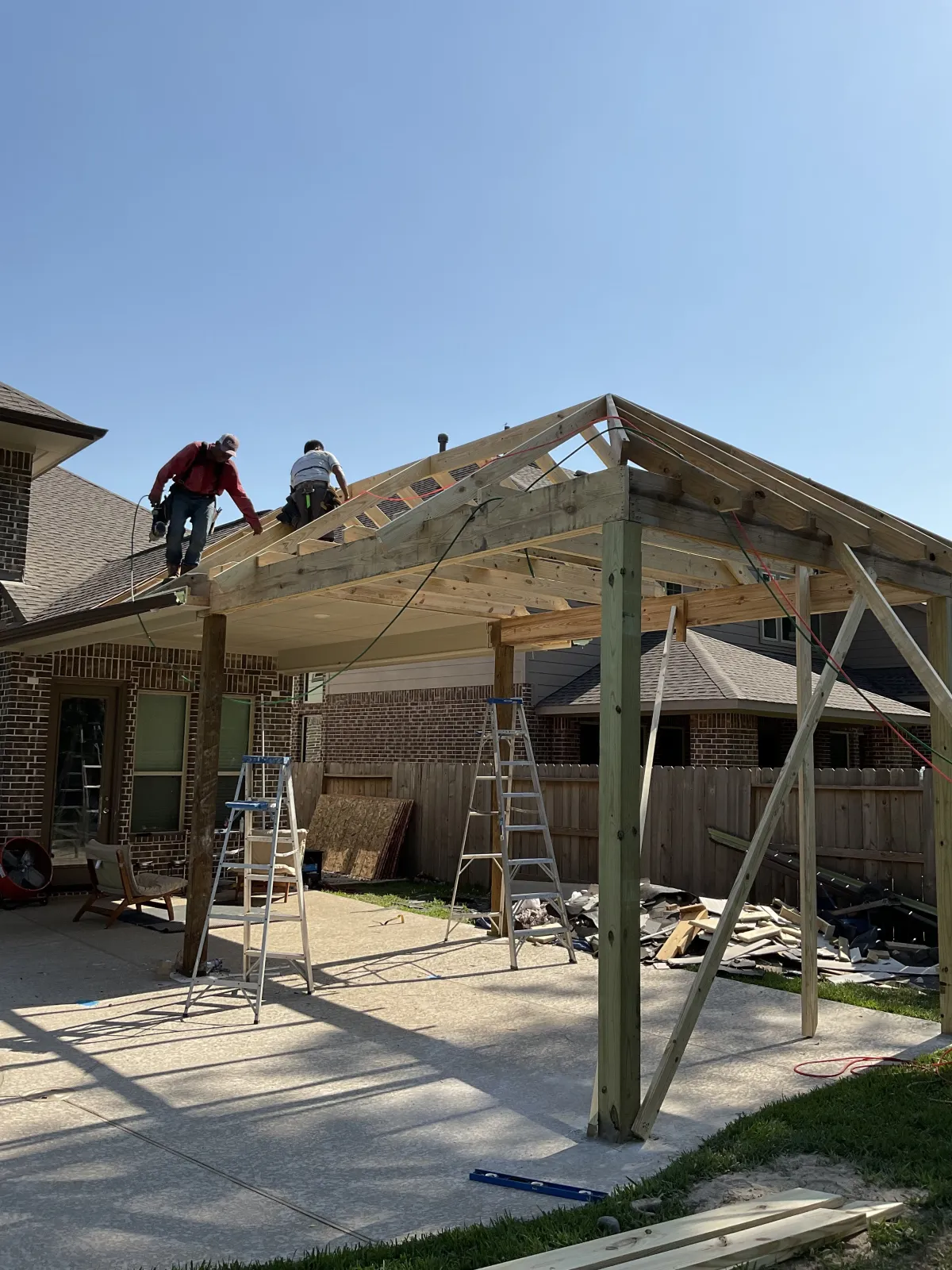 Partially framed covered patio structure with scaffolding and exposed roof beams behind a brick home
