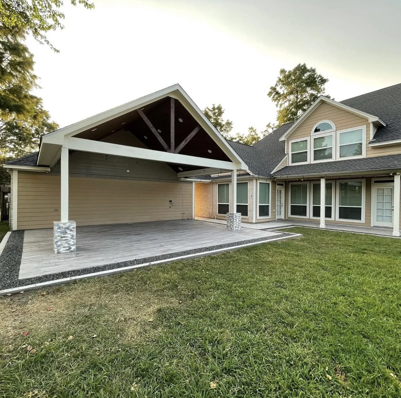 Completed large gabled covered patio with stained wood ceiling, exposed beam trusses, stone column bases, and composite decking