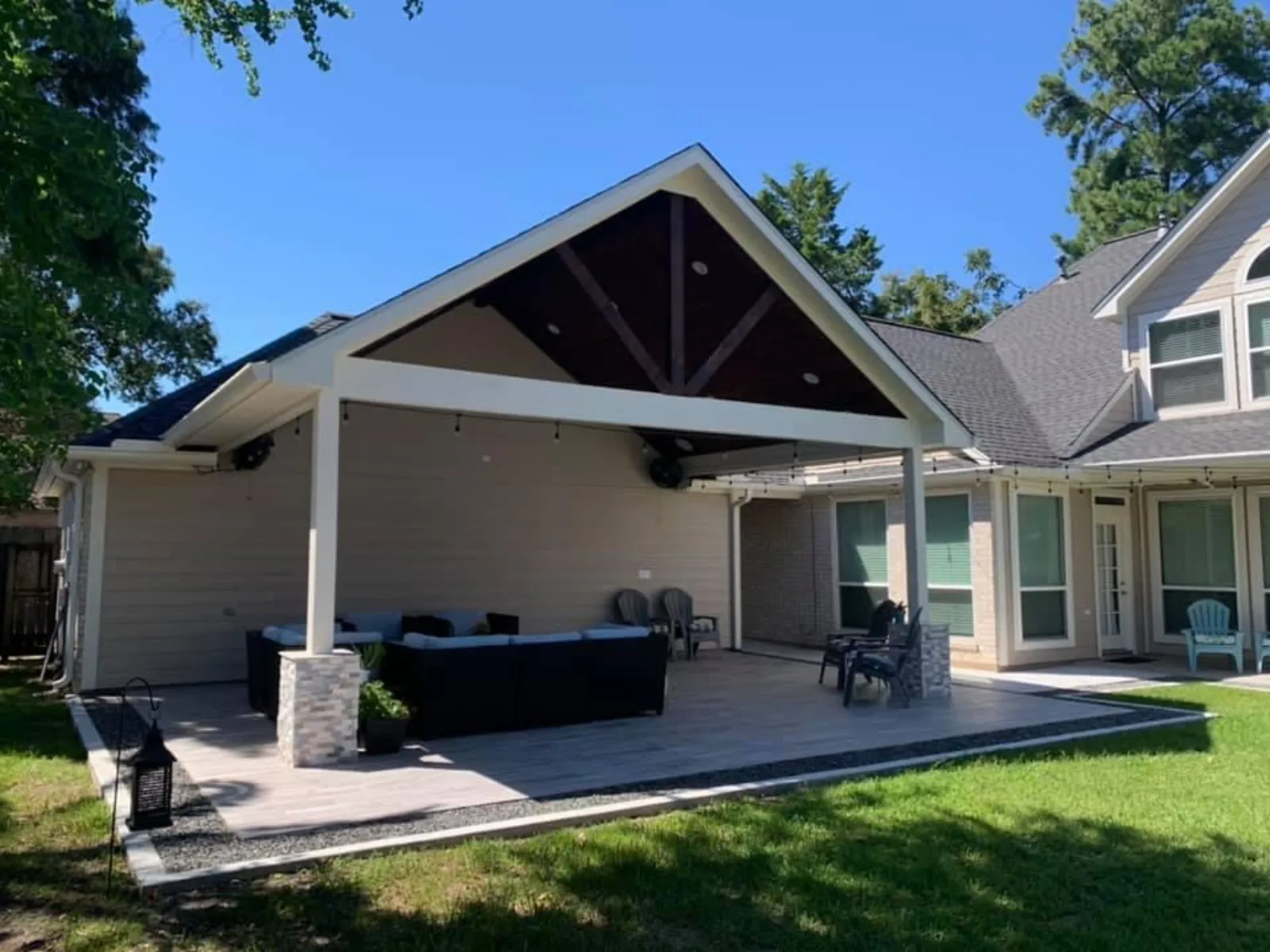 Furnished covered patio with a large sectional sofa, outdoor chairs, stone columns, stained beam ceiling, and string lights