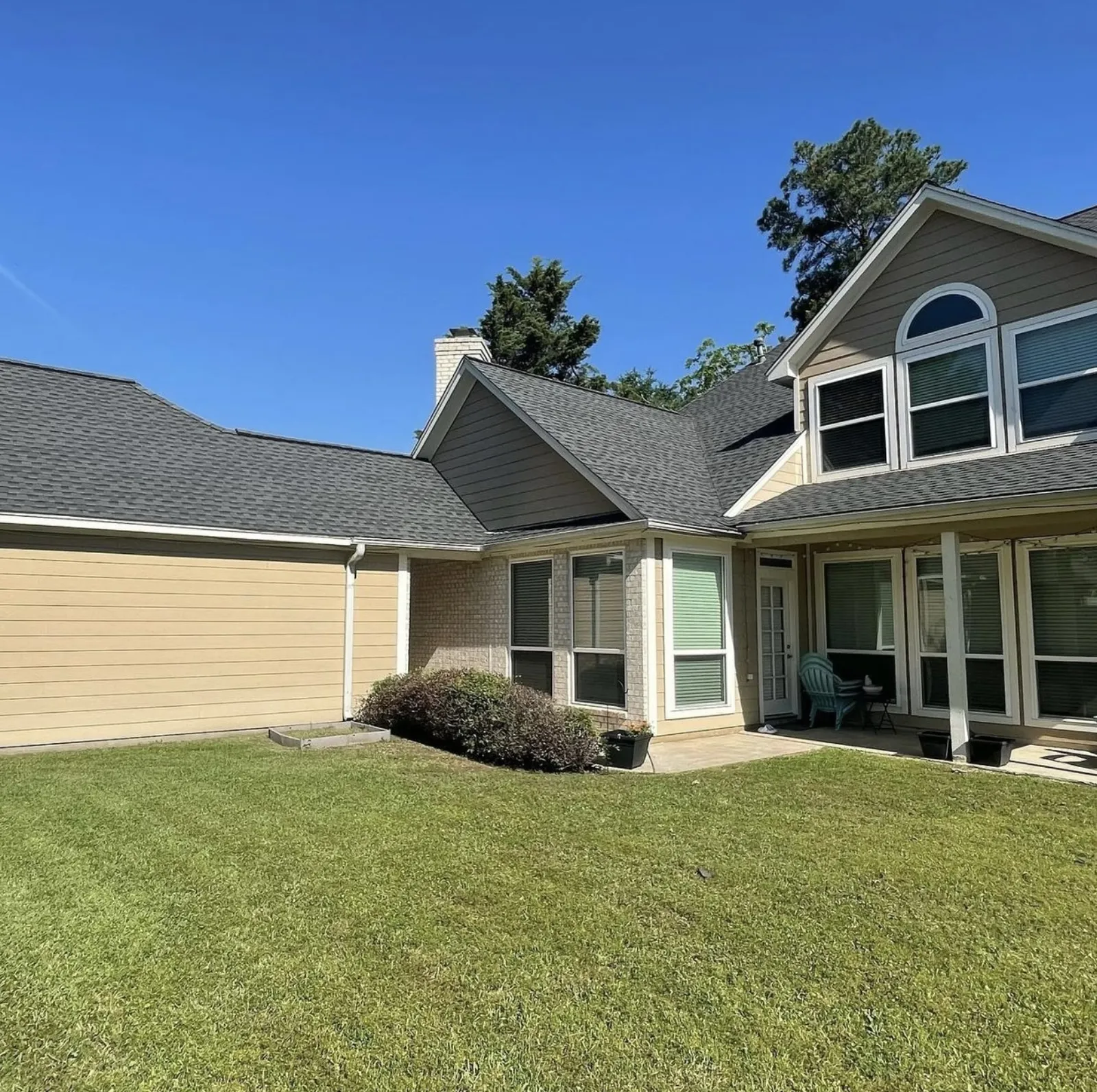 Rear view of a two-story home with a small existing patio and green lawn before a covered patio addition