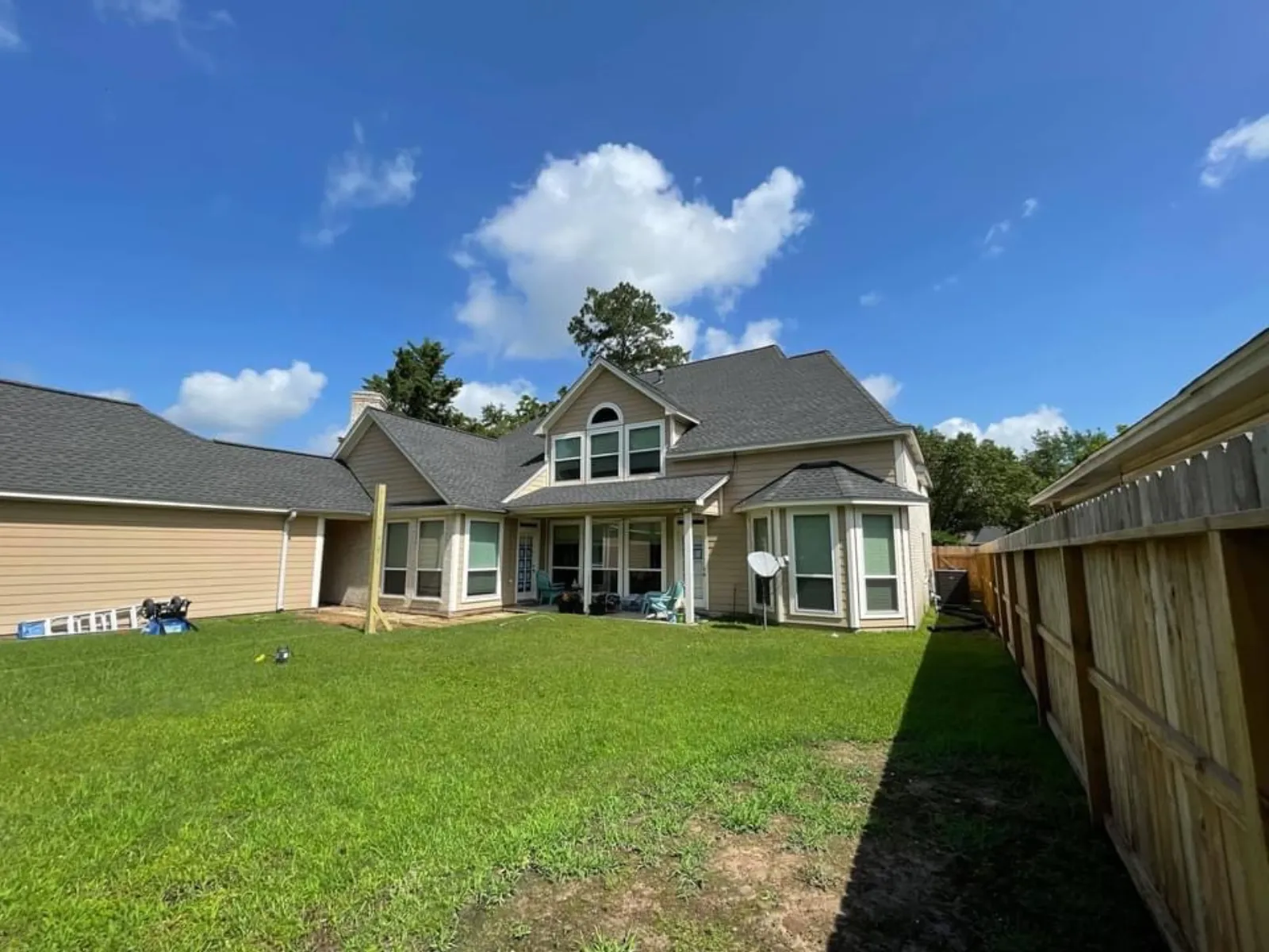 Wide backyard view of a two-story home with a small existing patio and a single wood post marking the start of construction